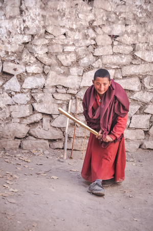 Hemis, Ladakh - circa November 2011: Young monk dressed in red clothes holds self-made wooden cricket bat and plays cricket at Tibetan Buddhist monastery in Hemis, Ladakh. Documentary editorial.のeditorial素材