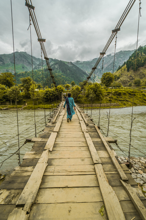 A woman crossing river Indus on dangerously looking bridge in Pakistan.の写真素材