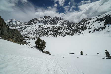 Pacific Crest Trail. A snow covered mountain range with a lake in the foreground. The sky is clear and blue with a few cloudsの写真素材