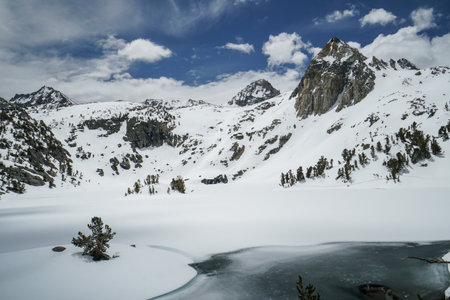 Pacific Crest Trail. A snow covered mountain range with a lake in the foreground. The sky is clear and blueの写真素材