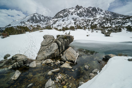 A mountain range with a small body of water in the foreground. The water is murky and the rocks are scattered around it. The scene is peaceful and sereneの写真素材