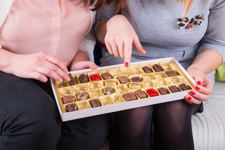 Womens on the couch eating a box of sweet chocolatesの写真素材