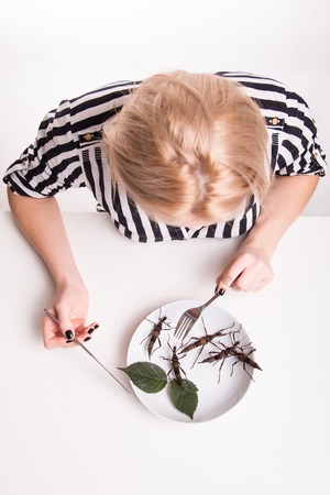 Woman eating big insects with a fork in a restaurantの写真素材