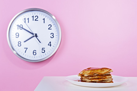 American pancakes with maple syrup on a pink background with a clockの写真素材