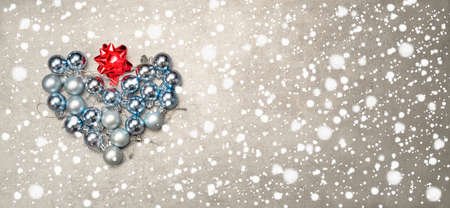 Christmas baubles in a gray and blue arranged in a heart shape on a winter backgroundの写真素材