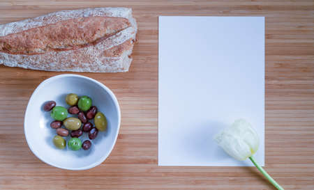 white card with space for text on a wooden kitchen countertop with bread and olivesの写真素材