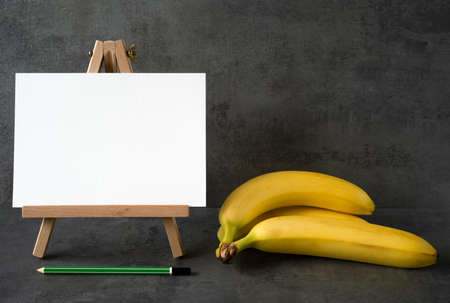 wooden easel with white board with space for text with green pencil and bananas in the kitchenの写真素材