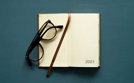 2021 calendar with space for text, brown bookmark, brown glasses, on a painted background, photo from aboveの写真素材