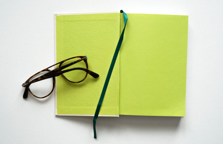 notebook with space for text, green paper, green bookmark, brown glasses, white background, canvas texture, top photoの写真素材