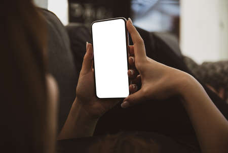 Girl using smartphone blank screen frameless modern design while lying on the sofa in home interiorの写真素材