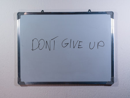 Whiteboard showing DONT GIVE UP message on clean white wall background representing motivation, perseverance and resilienceの写真素材