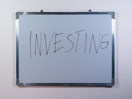 Whiteboard showing INVESTING concept on clean white wall background representing financial strategy, long term growth and marketsの写真素材
