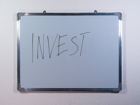 Whiteboard showing INVEST message on clean white wall background representing investment decision, finance and wealth buildingの写真素材