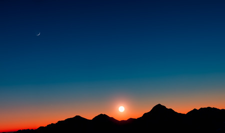 Sunset with mountains in silhouette with the moonの写真素材