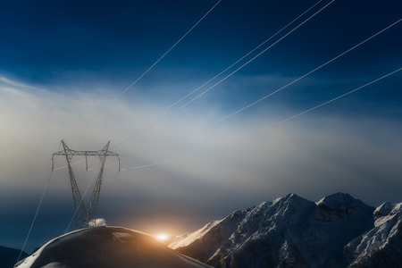 Pylons covered with snow in the high mountains carry energy downstreamの写真素材