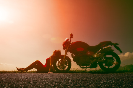 Woman sitting on the wheel of his motorcycle on the street alone in the sun.の写真素材