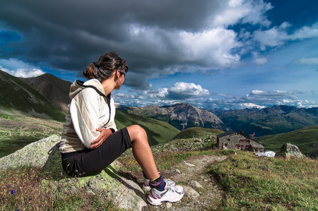 Woman sitting in the mountains observed an alpine hut and the view in the summerの写真素材