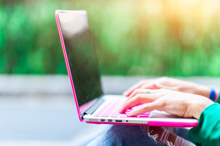 Detail of girl who writes on laptop computer outdoors in the street near a park in the cityの写真素材