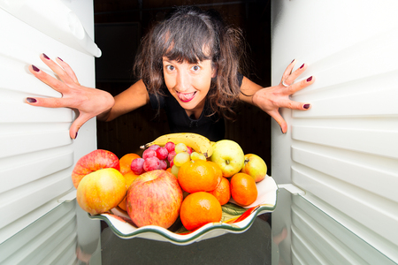 Woman opens the fridge and she is happy to see fruitsの写真素材