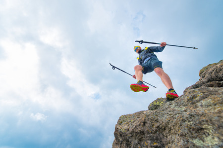 Male athlete falls over a cliff with sticks while practical training at the mountain trailの写真素材
