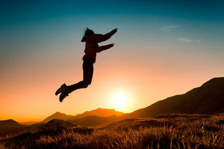 55/5000Girl jumps in the meadow during a sunset in the mountains.の写真素材