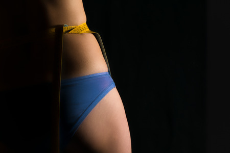 Girl in panty with centimeters on a waist on a black background.の写真素材
