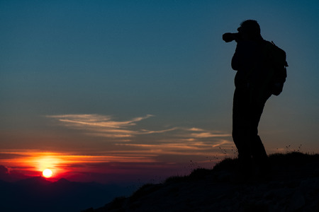 Photographing the sunset in the mountains. Photographer in silhouette.の写真素材