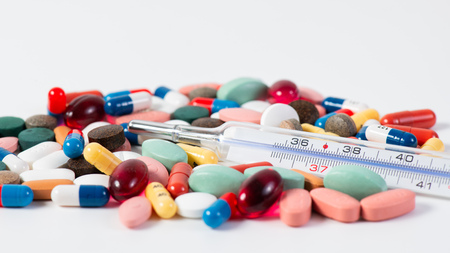 Fever thermometer with small medications on a white background.