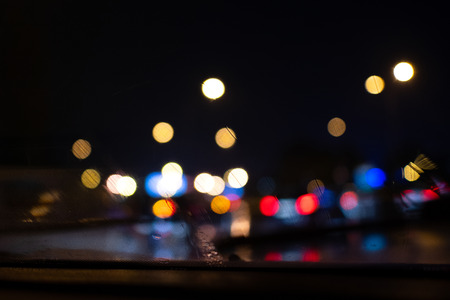 From a car windshield with windshield wipers in action. Blurry lights outside in the night.