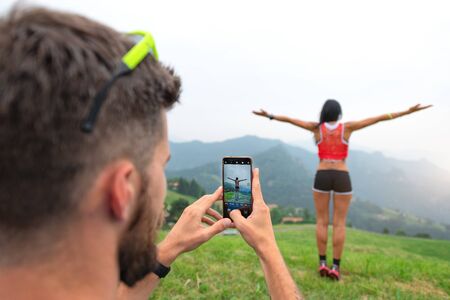 Man photographs a sporty woman with his smartphone during a mountain excursion