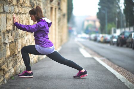 Young girl practices stretching in the city on a wall of a building