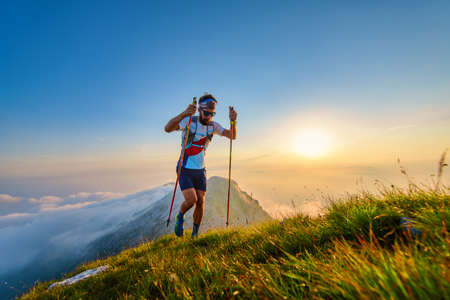 Man with poles in the mountains with sunset behindの写真素材