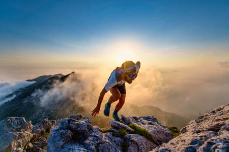 Sky runner man uphill on rocks at sunset