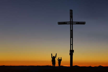 Mom with child on top of the mountain near the cross raise their arms in victoryの写真素材