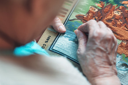 Hands of an elderly woman working with coloring threads and needle with half-stitch techniqueの写真素材
