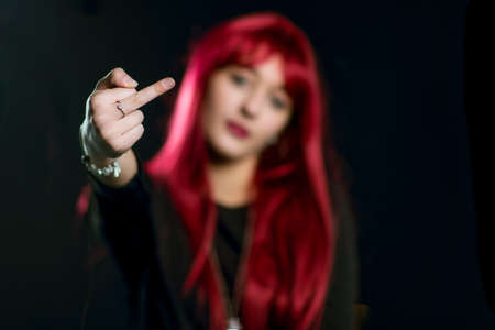 A girl with red hair does the middle finger on a black background