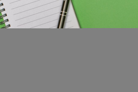 A notebook with a blank page and a pen resting on it on green matte cardboard