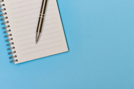A notebook with a blank page and a pen resting on it on light blue matte cardboardの写真素材