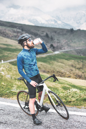 A road cyclist in the mountains stops and drinks from his water bottleの写真素材