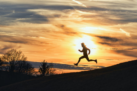 Sporty man runs down hill in silhouette at sunsetの写真素材