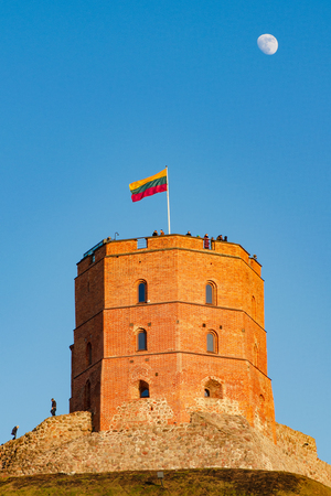 Gediminas' Tower or Castle, the remaining part of the Upper Castle in Vilnius, Lithuania with lithuanian flag waving on a green hill, blue sky and moonのeditorial素材