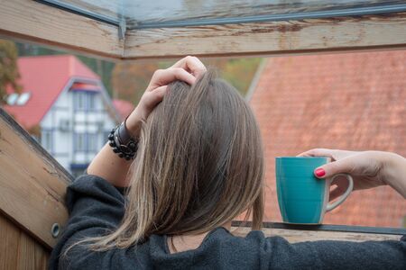 Woman with a mug looking through the window at a rainy dayの写真素材