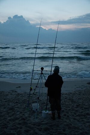 Night fishing, fisherman on the shore with sunset and sea on background, sport, competition on the Baltic Sea, verticalの写真素材