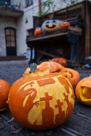 Spooky Halloween pumpkins, Jack O Lantern, with drawings of ghost, crosses and devil on a wooden floor and some old floor, verticalの写真素材