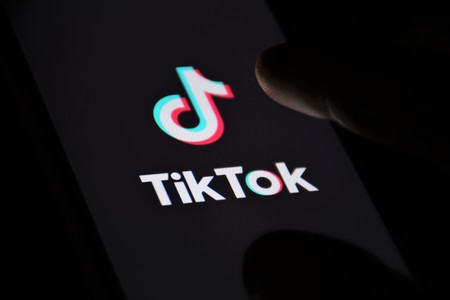 TikTok logo, app icon, logo displayed on a modern smartphone with fingerのeditorial素材