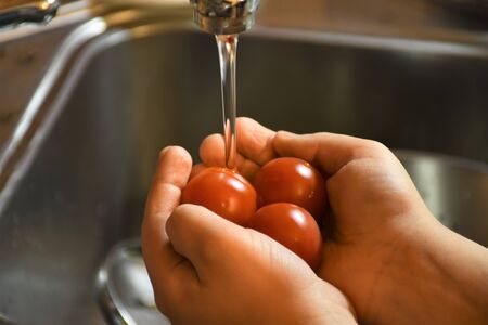 Hands of young boy washing fresh tomatoes under tap water in the kitchenの写真素材