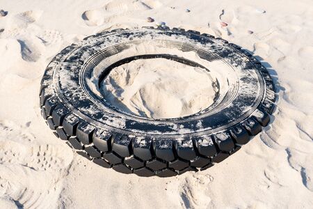 Big black rubber tire left on a sandy beach, environment pollution concept