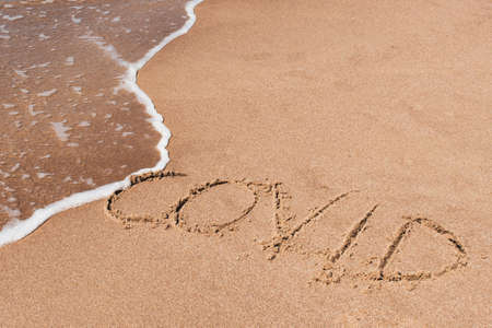 Covid free, stop Covid, safe beach and holiday, word written on the sand with wave washing and...