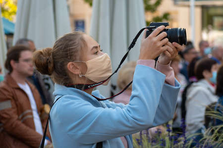 Beautiful girl with mask taking photos with camera during Covid or Coronavirus outbreak in a  public...