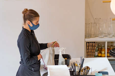 Pretty waitress with mask cleaning and disinfecting cutlery in bar, cafÃ© or restaurant during Coronavirus or Covid outbreakのeditorial素材